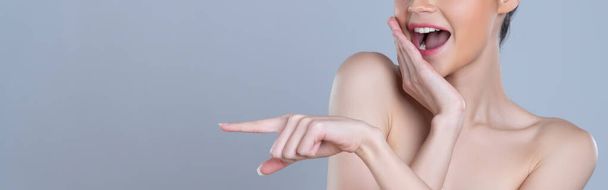 Detailní okouzlující krásná žena s perfektní make-up čisté kůže ukazující prstem v copyspace izolované pozadí. Propagace naznačená konceptem gesta ruky pro reklamu na výrobky pro péči o pleť. - Fotografie, Obrázek