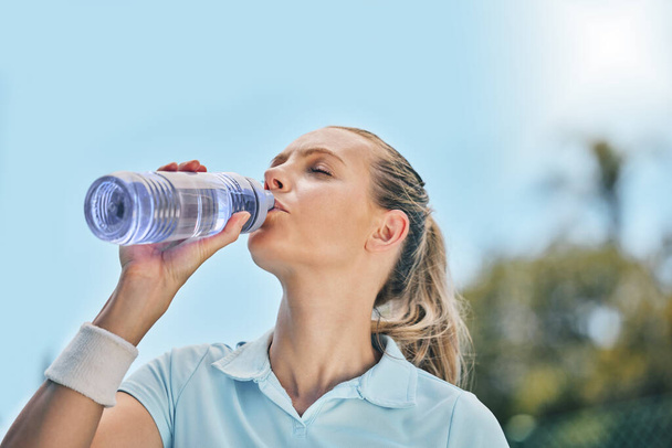 Woman, tennis player and drinking water for hydration after workout, exercise or intense training in nature. Sporty female with bottle for refreshing drink to stay hydrated during sports exercising. - Foto, imagen