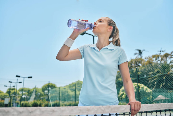 Frau, Tennis und Trinkwasser zur Hydratation nach dem Training, Sport oder intensivem Training auf dem Platz. Sportliches Weibchen mit Flasche für erfrischendes Getränk, Durst oder Feuchtigkeit beim Sport. - Foto, Bild