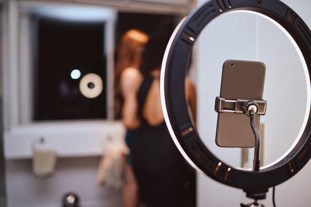 ring light, phone and woman influencer equipment with friends live streaming getting ready. Night, creative gen z content and internet production tech with blurred background and mockup in a home. - 写真・画像