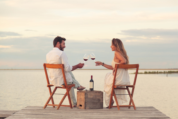 ζευγάρι πόσιμο κόκκινο κρασί στην παραλία σε μια προβλήτα - Φωτογραφία, εικόνα