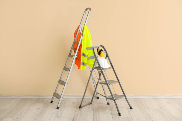 Stepladders with builder's equipment and reflective vests near beige wall - Foto, immagini