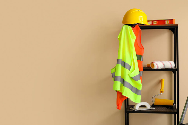 Shelving unit with builder's equipment and reflective vests near beige wall - Foto, immagini