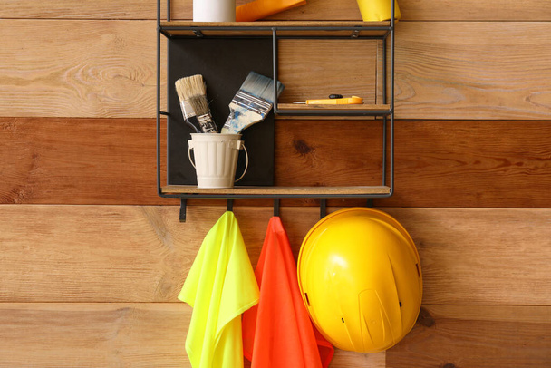 Shelf with builder's supplies and reflective vests on wooden wall - 写真・画像