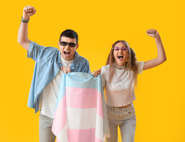 Jeune couple avec drapeau transgenre criant sur fond jaune - Photo, image