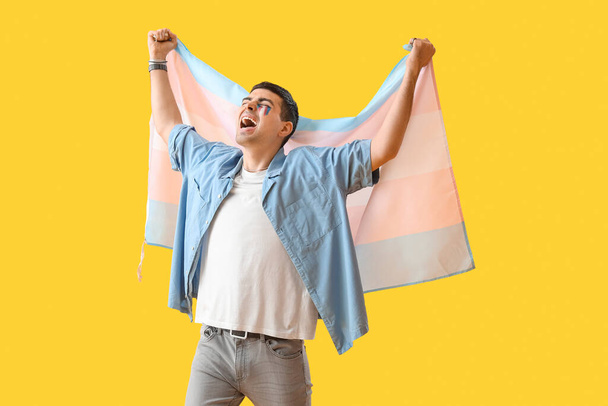 Молодой человек с трансгендерным флагом кричит на жёлтом фоне - Фото, изображение