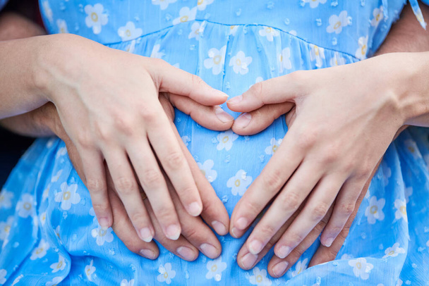 mãos masculinas e femininas mostrando forma do coração na barriga da mulher grávida. Conceito de família, gravidez e maternidade - Foto, Imagem