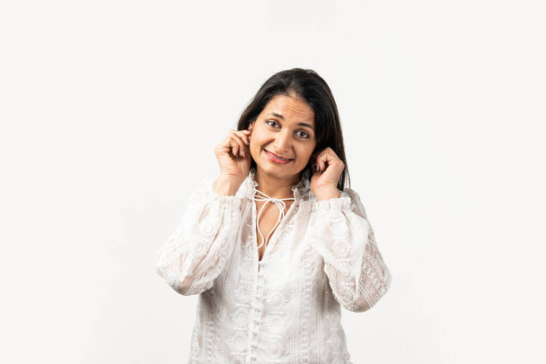 Mid aged Indian woman in a sorry pose, holding both ears. Standing isolated over white background - Foto, immagini