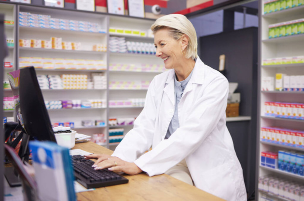 Pharmacy, computer database and senior woman pharmacist working of medicine research. Pharmaceutical data, typing and healthcare employee smile checking online information for medical prescription. - Foto, Imagem