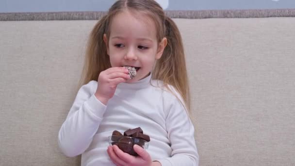 happy little girl enjoying eat Glass bowl with chocolates Sweet snack. High quality 4k footage - Felvétel, videó