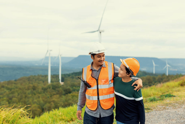 Ingenieur met zijn zoon op een windmolenpark op een heuvel of berg op het platteland. Progressief ideaal voor de toekomstige productie van hernieuwbare, duurzame energie. Energieopwekking uit windturbine. - Foto, afbeelding