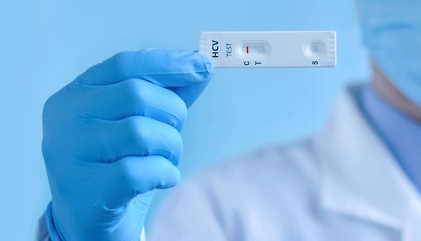 Врач в защитной маске и перчатках показывает быстрый лабораторный тест на вирус гепатита С (ВГС). Тест показывает отрицательный результат. - Фото, изображение