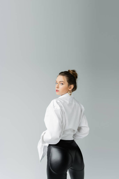 sexy woman in white shirt and black tight pants looking at camera isolated on grey - 写真・画像