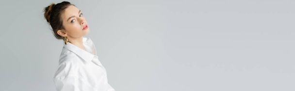 portrait of trendy woman with natural makeup posing in white oversize shirt isolated on grey, banner - Photo, Image