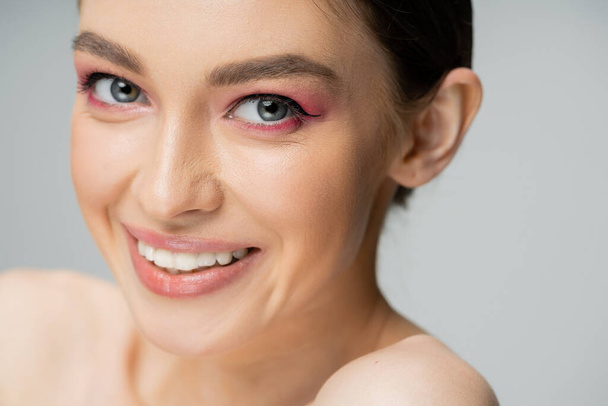 close up portrait of cheerful woman with makeup looking at camera isolated on grey - 写真・画像