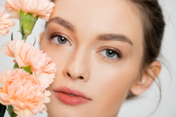 close up portrait of pretty woman with clean skin and natural makeup near peach carnations isolated on grey - Foto, immagini