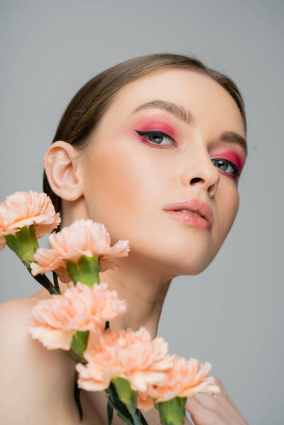 portrait of young woman with perfect skin and makeup looking at camera near fresh flowers isolated on grey - Photo, image