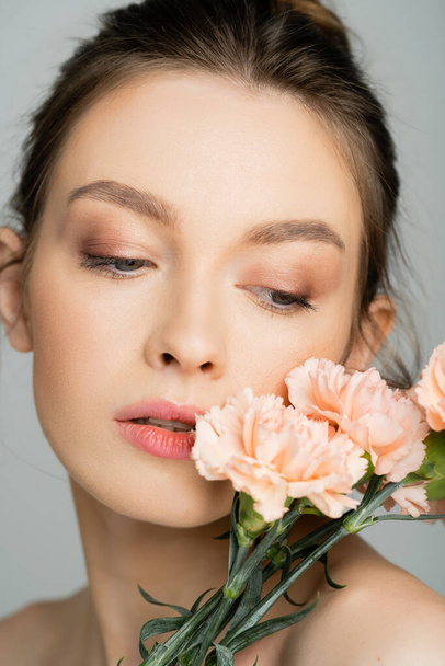 Portrait of woman with natural makeup posing with carnations isolated on grey  - Fotoğraf, Görsel