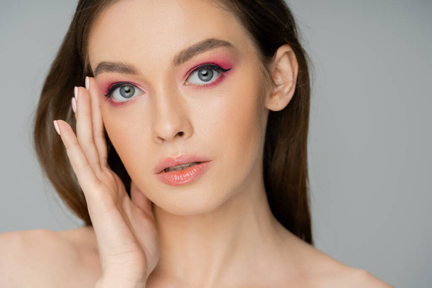 Portrait of young woman with pink makeup touching face isolated on grey  - Foto, immagini