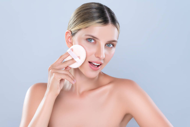 Alluring beautiful female model applying powder puff for facial makeup concept. Portrait of flawless perfect cosmetic skin woman put powder foundation on her face in isolated background. - Foto, imagen