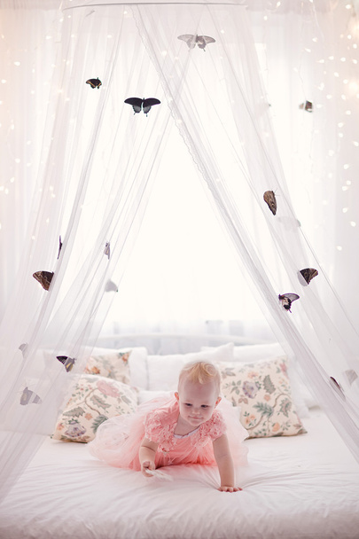 Pretty little girl with butterflies all around white bed. - Valokuva, kuva