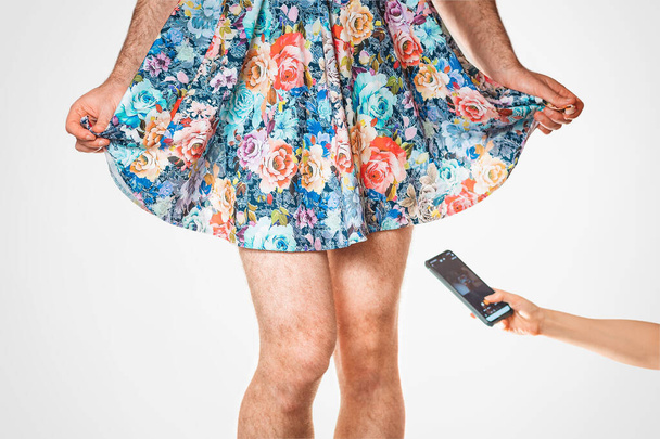 ΛΟΑΤ. Μια γυναίκα τραβάει κρυφά το εσώρουχο κάτω από τη φούστα ενός τρανσέξουαλ άντρα. Πλευρική άποψη, κοντινό πλάνο. Η έννοια της ηδονοβλεψίας και της σεξουαλικής διαστροφής. - Φωτογραφία, εικόνα