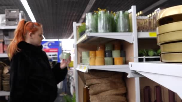Shelves in a store with interior and home decor items. In the background, out of focus, a girl chooses a glass flowerpot. - Filmmaterial, Video