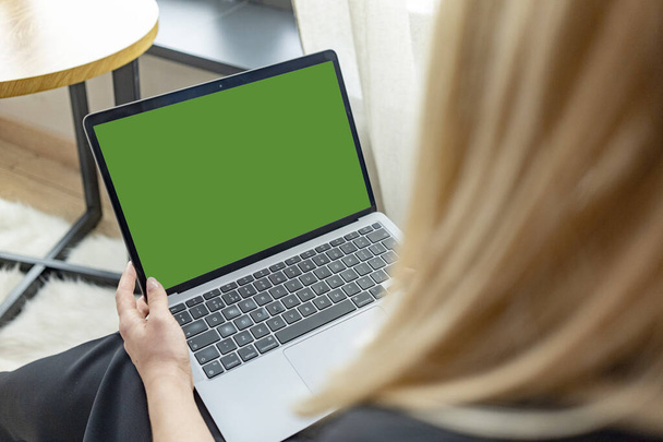 Una joven sostiene un ordenador portátil que mira una maqueta de una pantalla de ordenador verde en línea entrenamiento de PC. Vista de cerca sobre el hombro. Foto de alta calidad - Foto, Imagen