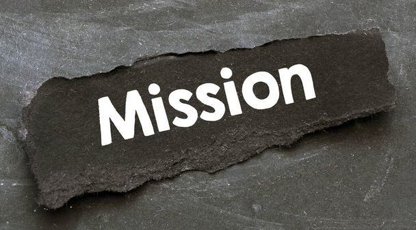 Wort MISSION auf einem schwarzen Blatt Papier auf schwarzem Hintergrund. - Foto, Bild