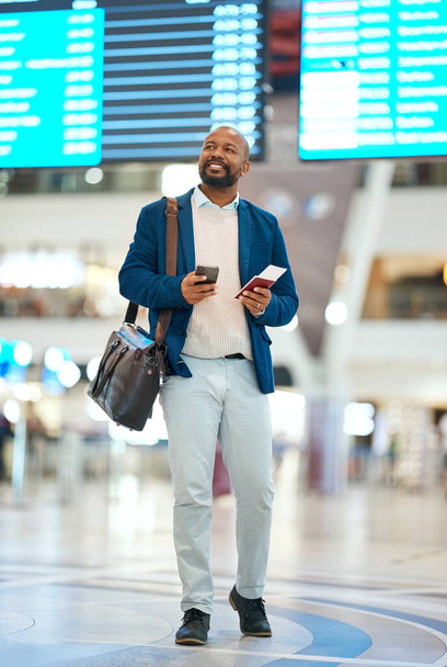 Black man with phone, airport and flight schedule, walking in terminal, holding ticket and passport for business trip. Smile, travel and happy businessman checking international destination online - Photo, image