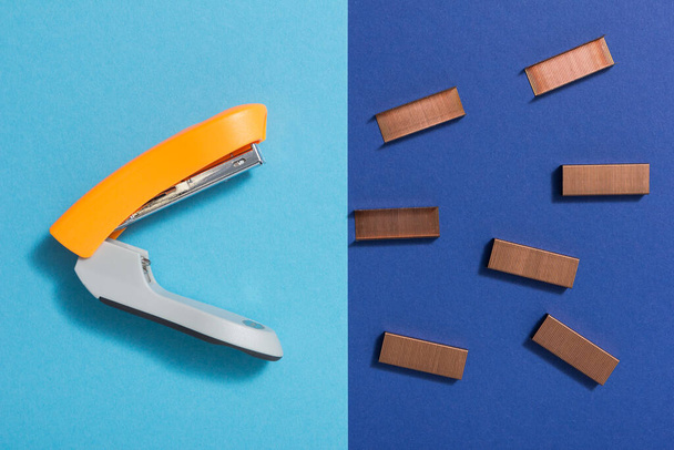 Top view of an open stapler with its staples in front of it. Background in two shades of blue. - Fotó, kép