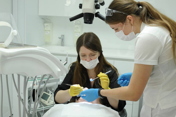 Жінка-пацієнтка відкриває рот під мікроскопом зубів і професійний стоматолог, який тримає інструменти стоматолог лікар і медсестра лікує зуби пацієнту за допомогою мікроскопа
 - Фото, зображення