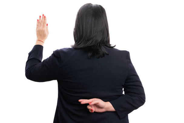 Взрослая женщина-предприниматель делает нечестный жест со скрещенными за спиной пальцами в элегантном повседневном костюме, как корпоративная концепция, изолированная на белом фоне - Фото, изображение