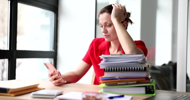 ビジネスの女性は、フォルダを持つオフィスのテーブルでスマートフォンで作業散乱。情報疲労症候群とインターネットサーフィン中毒の概念 - 映像、動画
