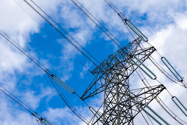 High-voltage pylon against a blue sky with a slight cloud cover. High voltage transmission lines silhouette - Fotografie, Obrázek