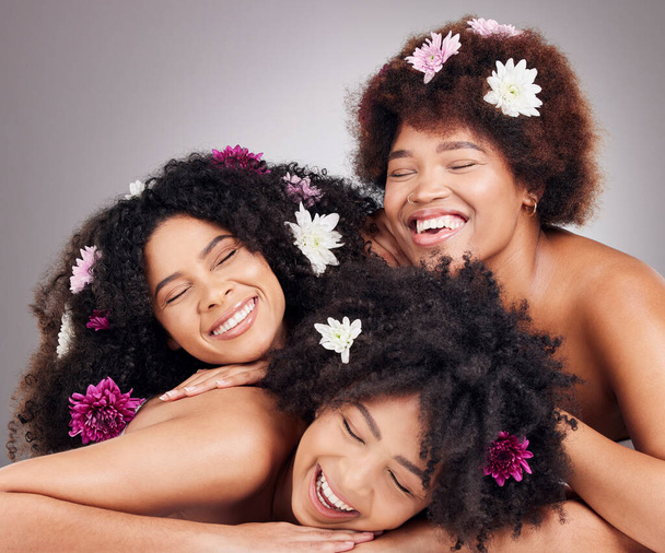 Friends, hair care and black women with flowers in studio isolated on a gray background. Floral cosmetics, organic makeup and face of group of girls or models with plants for aesthetic and beauty - Fotografie, Obrázek