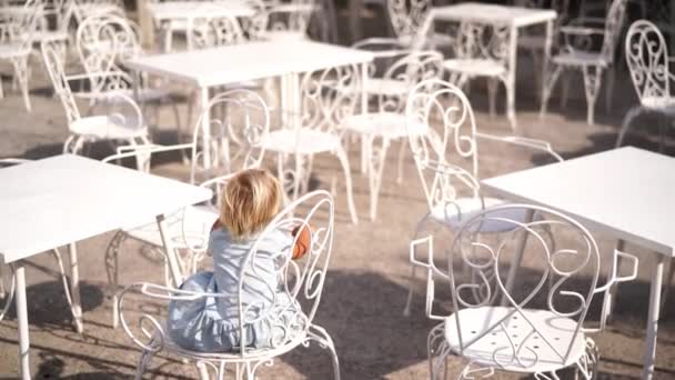 Little girl climbed out onto a chair with a back and spins on it, trying to swing. High quality 4k footage - Imágenes, Vídeo