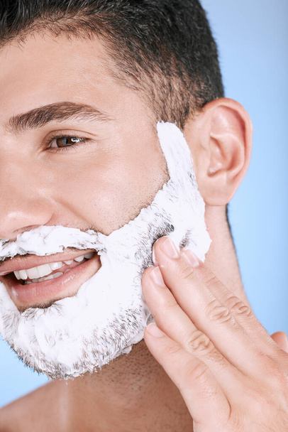 Shaving, foam and smile on face, man with hand on beard, product placement and mock up in studio. Shave cream facial, luxury hair and skincare for male model with smile, isolated on blue background - Zdjęcie, obraz