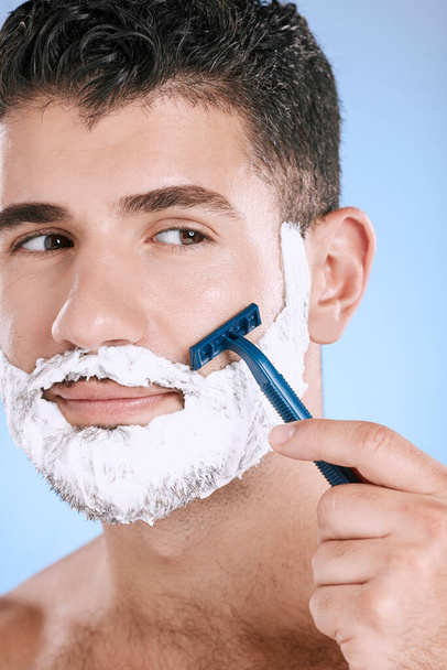 Ξύρισμα, γενειάδα και καλλυντικός άντρας με κρέμα για περιποίηση σε μπλε φόντο. Δερμάτινη περιποίηση, ομορφιά και μοντέλο με ξυράφι για ξύρισμα μαλλιών στο πρόσωπο με αφρό για καθαρή όψη προσώπου σε φόντο. - Φωτογραφία, εικόνα