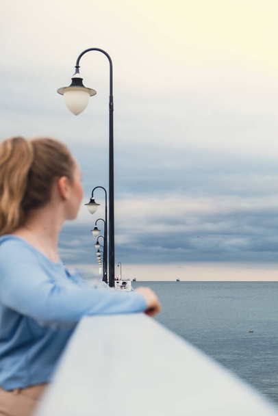 Eine junge Frau, die auf einem Holzsteg steht, verschwimmt mit dem Hintergrund am Strand. Attraktive Frauen genießen das Reisen am Meer und das Konzept des aktiven Lebensstils. Frühling. Wellness Wohlbefinden psychische Gesundheit innerer Frieden Langsames Leben digitale Entgiftung - Foto, Bild