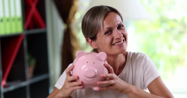 Mulher alegre feliz segurando banco porquinho nas mãos. Poupança de investimento em dinheiro e economia confiável - Filmagem, Vídeo