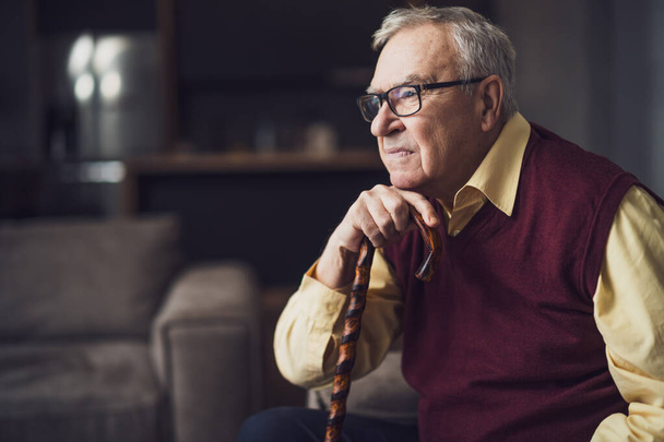 Ein ängstlicher und besorgter älterer Mann sitzt in seinem Haus im Bett. Porträt eines älteren Mannes mit Gehstock. - Foto, Bild