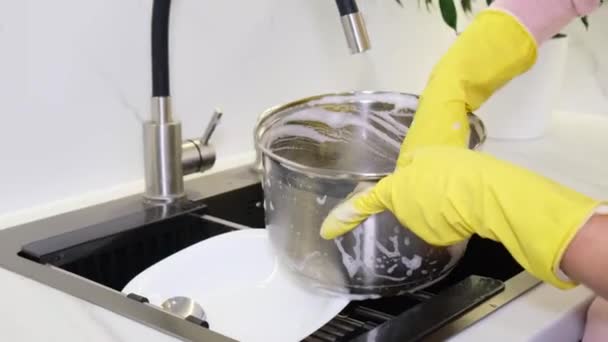 Χέρια γυναίκας με λαστιχένια γάντια που πλένει μια μεταλλική κατσαρόλα με σφουγγάρι. Κοντινό πλάνο πλυσίματος πιάτων στο νεροχύτη - Πλάνα, βίντεο