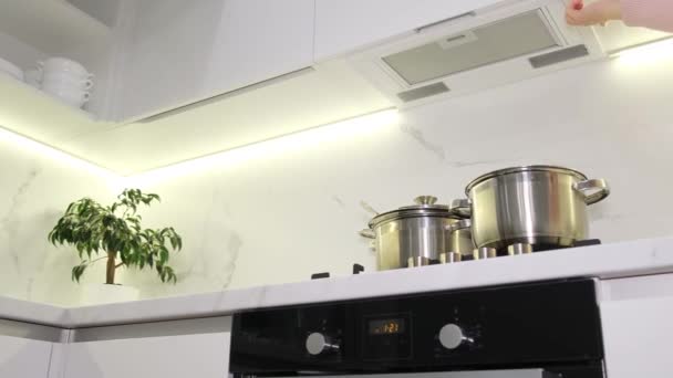 Vrouwelijke handen drukken op de knop om de ventilatie op het fornuis in de keuken aan te zetten. De stoom gaat de keukenkap in.. - Video