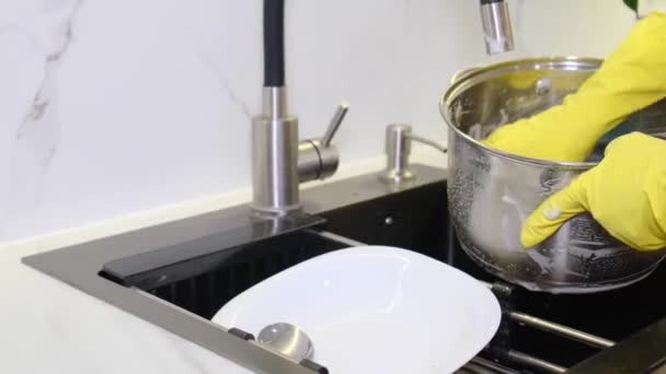 Close-up of woman washing metal pot wearing rubber gloves and sponge. The woman gradually washes the pot with water. Clean dishes in the kitchen. - Filmagem, Vídeo