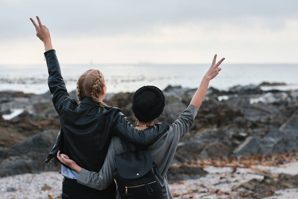 Women, back and friends at beach with peace sign, bonding and hugging. Freedom, travel and girls or females with v gesture or emoji, embrace and enjoying quality time together by seashore or ocean. - Photo, Image