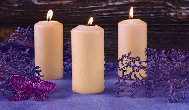 Burning candles and purple orchid flower. Dried flowers as a decoration. Romantic composition on a dark wooden background. - Foto, afbeelding
