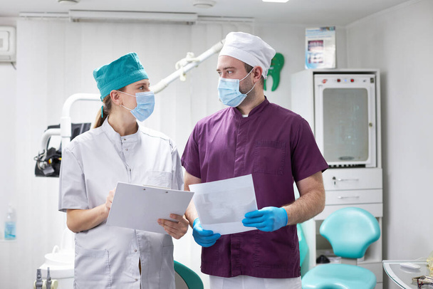 В современной стоматологической клинике опытный медицинский коллектив, состоящий из двух различных врачей-стоматологов, ортодонтов, осматривающих рентгеновскую панорамную пленку зубов и челюсти пациента. Стоматологическая практика. Люди - Фото, изображение