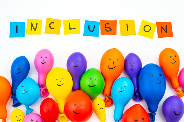 Ballonnen van verschillende kleuren op een wit oppervlak, en tekst "inclusie". Inclusie, acceptatie, integratie en diversiteit. - Foto, afbeelding