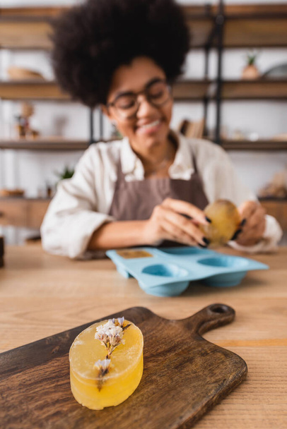 selective focus of herbal soap on chopping board near african american craftswoman smiling on blurred background - Фото, зображення